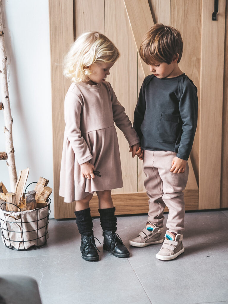 przykład jak można ubrać dziecko do przedszkola, rodzeństwo ubrane w strojmisiową, nową kolekcję jesienną. Beżowa sukienka, beżowe spodnie z prążkowanego materiału i czarny longsleeve.